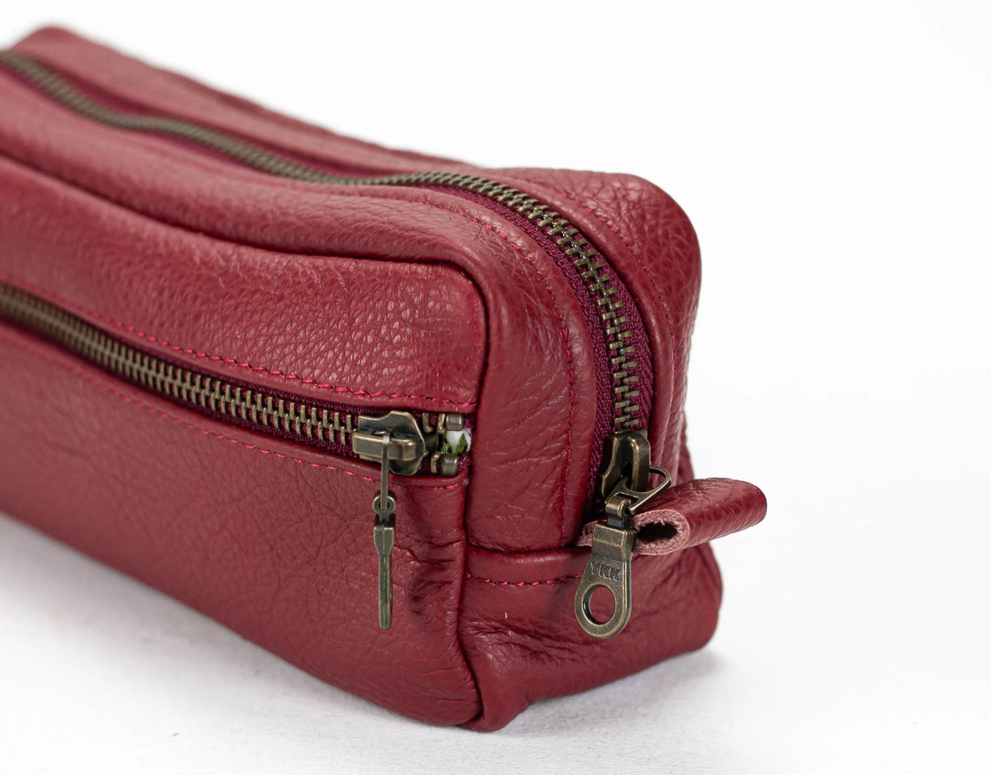 Red leather toiletry bag with gold zippers on a white background