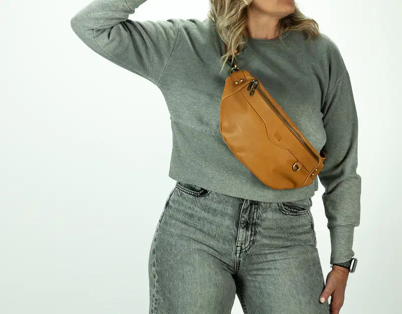 Person wearing a gray sweatshirt and jeans with a tan leather bag on a white background
