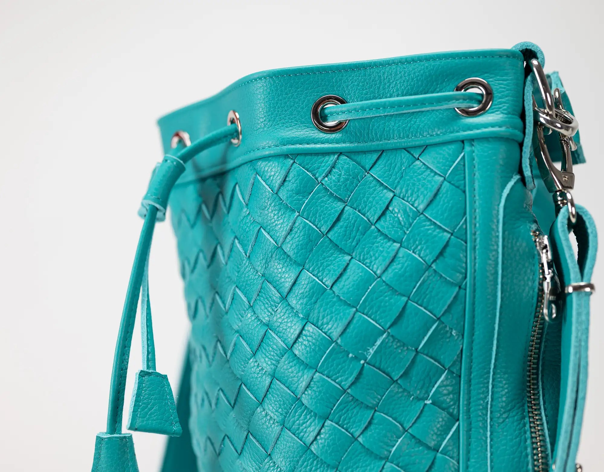 Turquoise woven leather handbag with drawstring and zipper on a white background