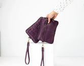 Purple quilted clutch with wrist strap held by a hand on a white background