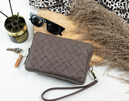 Brown quilted clutch bag on a white surface with sunglasses and other accessories.