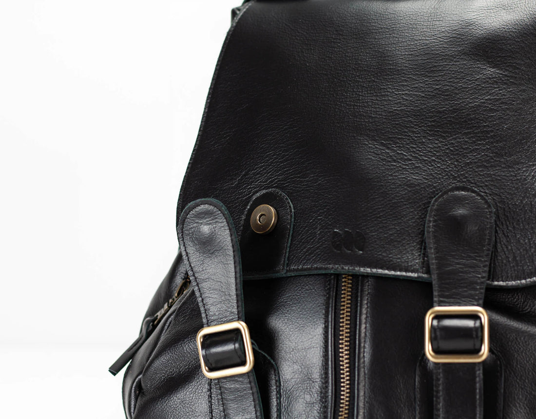 Close-up of a black leather backpack with gold buckles on a white background