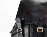 Close-up of a black leather backpack with gold buckles on a white background
