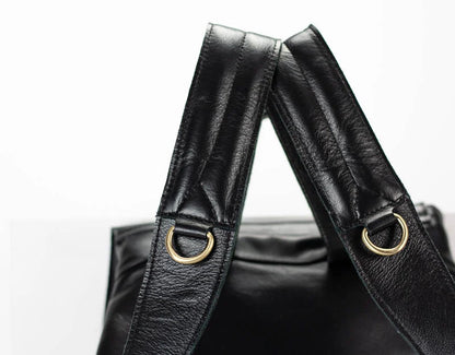 Black leather bag with gold hardware straps on a white background