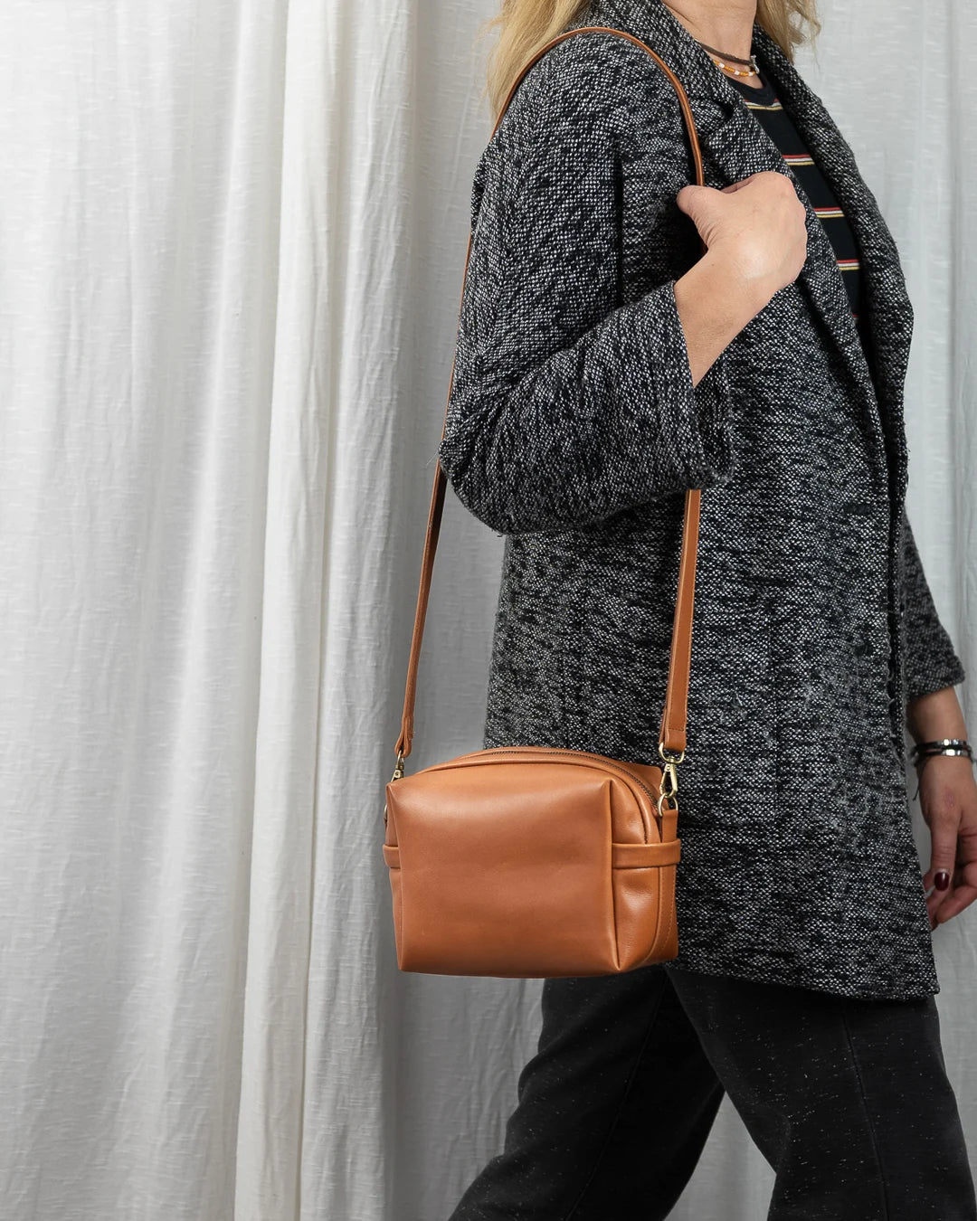 Person wearing a gray textured coat holding a brown leather handbag against a light background