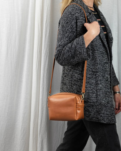 Person wearing a gray textured coat holding a brown leather handbag against a light background