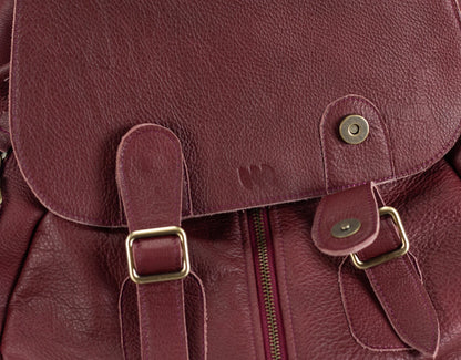 Close-up of a maroon leather bag with gold buckles and zipper.