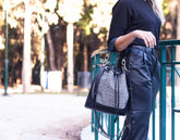 Person holding a black handbag with a textured pattern outdoors