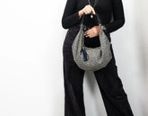 Person holding a gray textured handbag with tassels against a white background