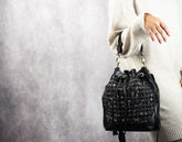 Black textured handbag held by a person wearing a light-colored sweater against a neutral background