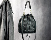 Black handbag with decorative elements hanging on a hook against a gray background