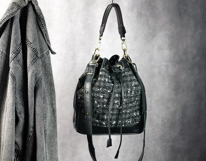 Black handbag with decorative elements hanging on a hook against a gray background