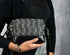 Person holding a black and silver patterned handbag against a gray background