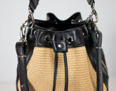 Black and straw handbag with metal accents on a light gray background