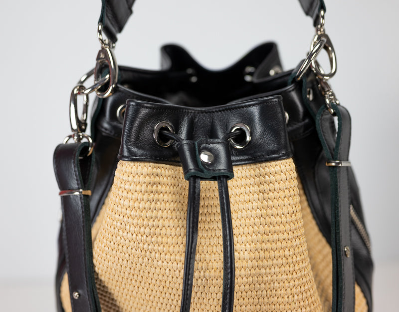Black and straw handbag with metal accents on a light gray background
