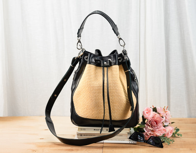 Black and beige handbag on a wooden surface with flowers and books in the background