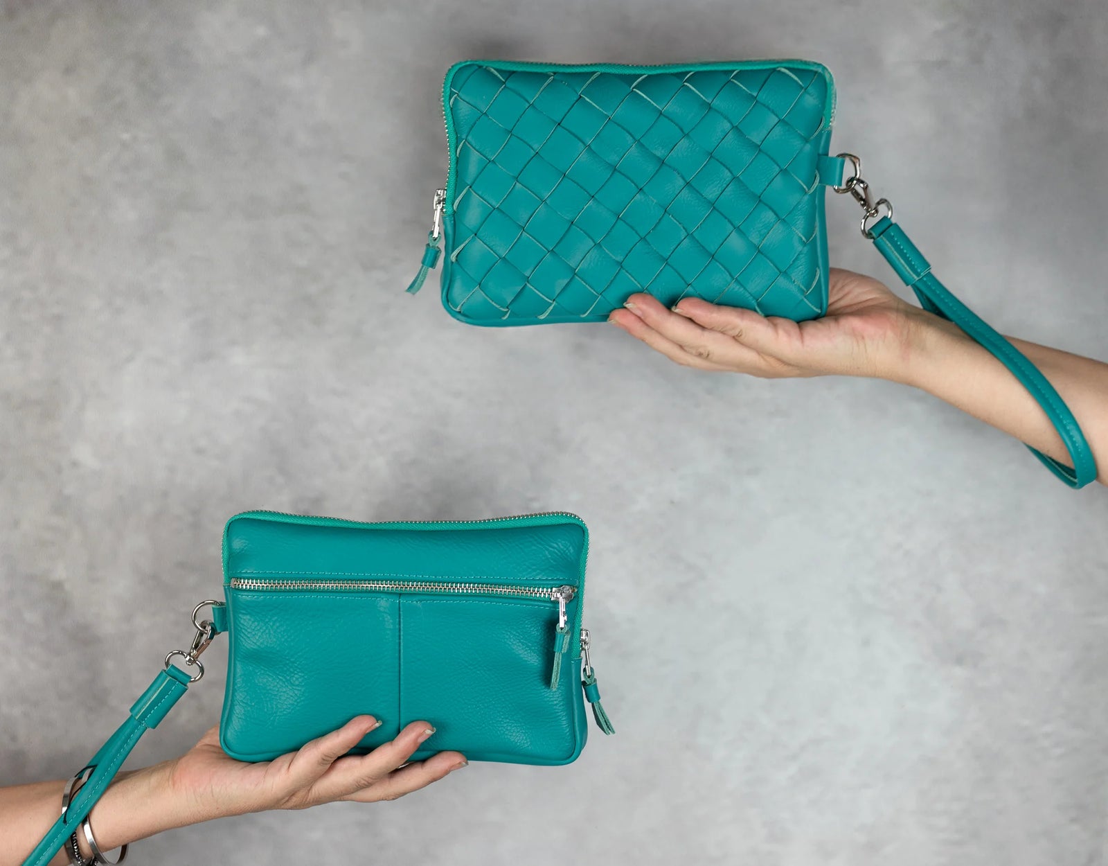 Two turquoise handbags being held against a gray background