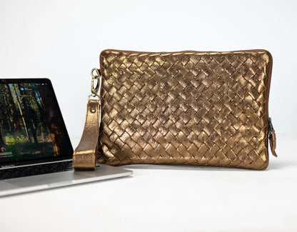 Gold woven clutch bag next to a laptop on a white background