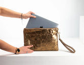Person holding a gold clutch with a laptop inside on a white background