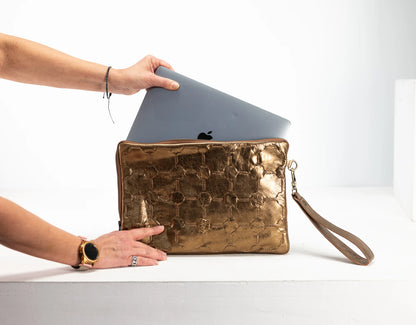 Person holding a gold clutch with a laptop inside on a white background