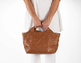 Brown textured handbag held by a person wearing a white outfit on a white background
