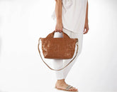 Person holding a brown leather handbag on a white background
