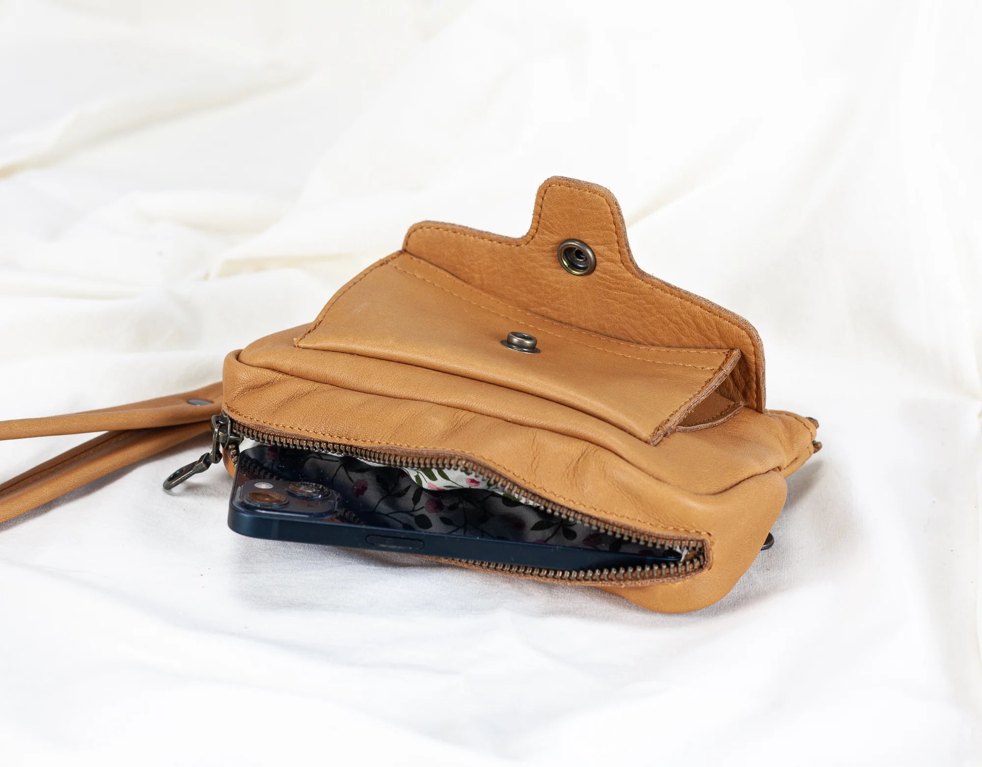 Tan leather crossbody bag with a zipper on a white background