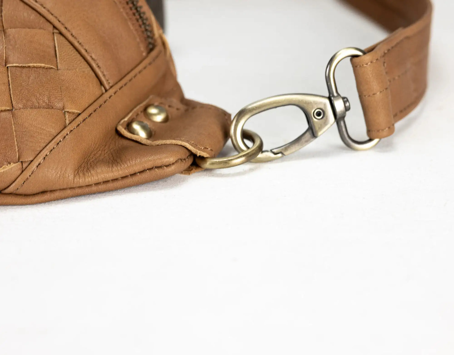 Close-up of a brown leather bag with a woven pattern and gold hardware on a white background