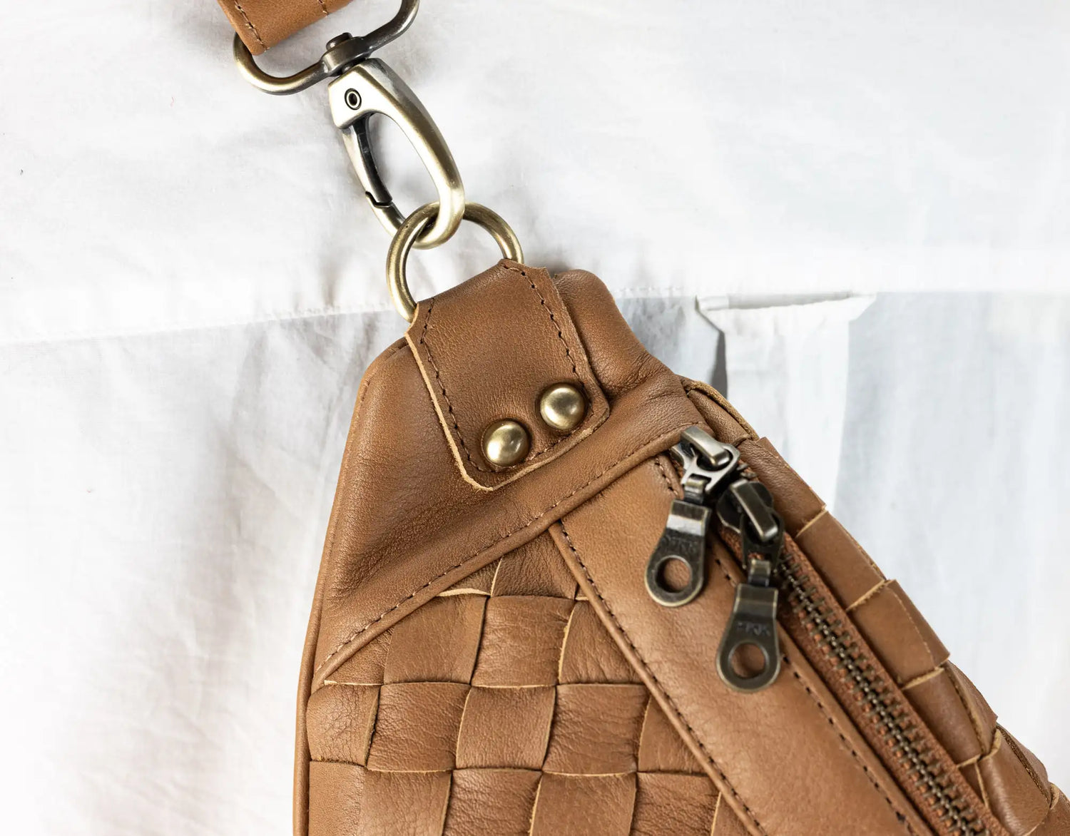 Brown woven leather bag with gold zipper and hardware on a white background