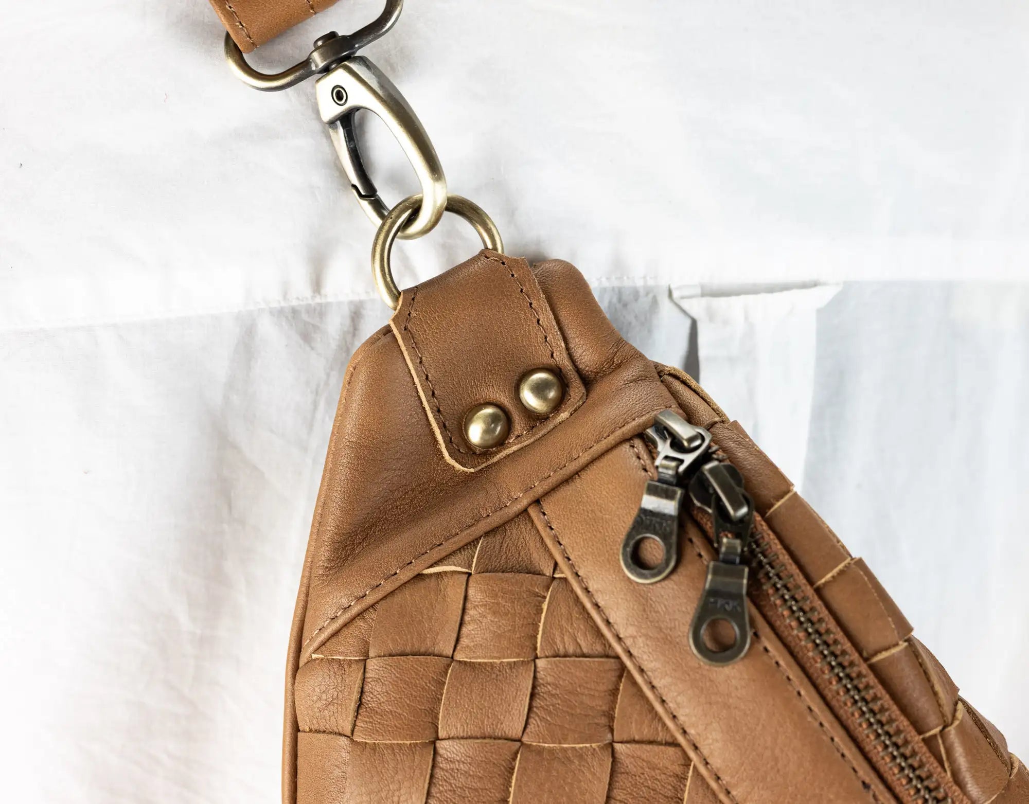 Brown woven leather bag with gold zipper and hardware on a white background