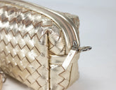 Gold woven handbag with a zipper on a light gray background