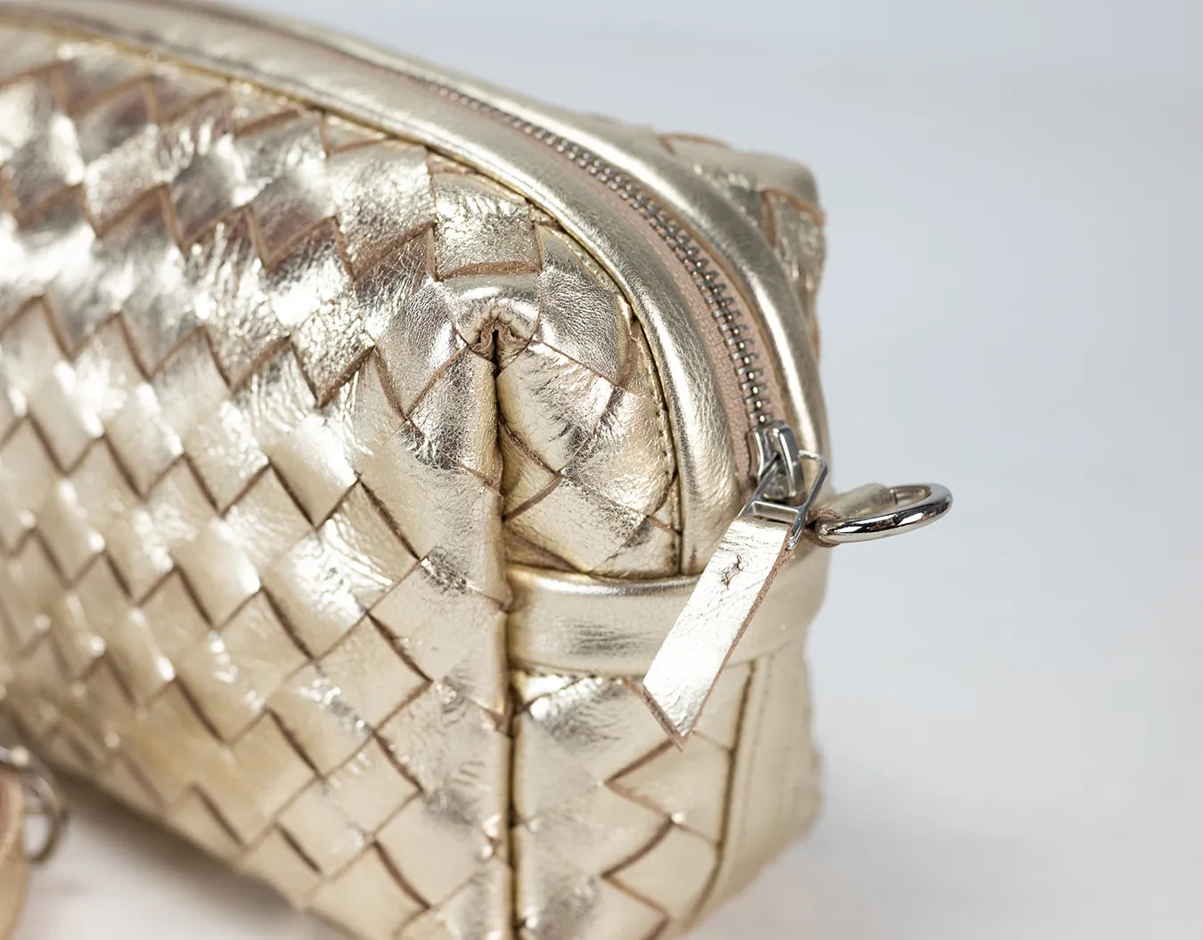 Gold woven handbag with a zipper on a light gray background