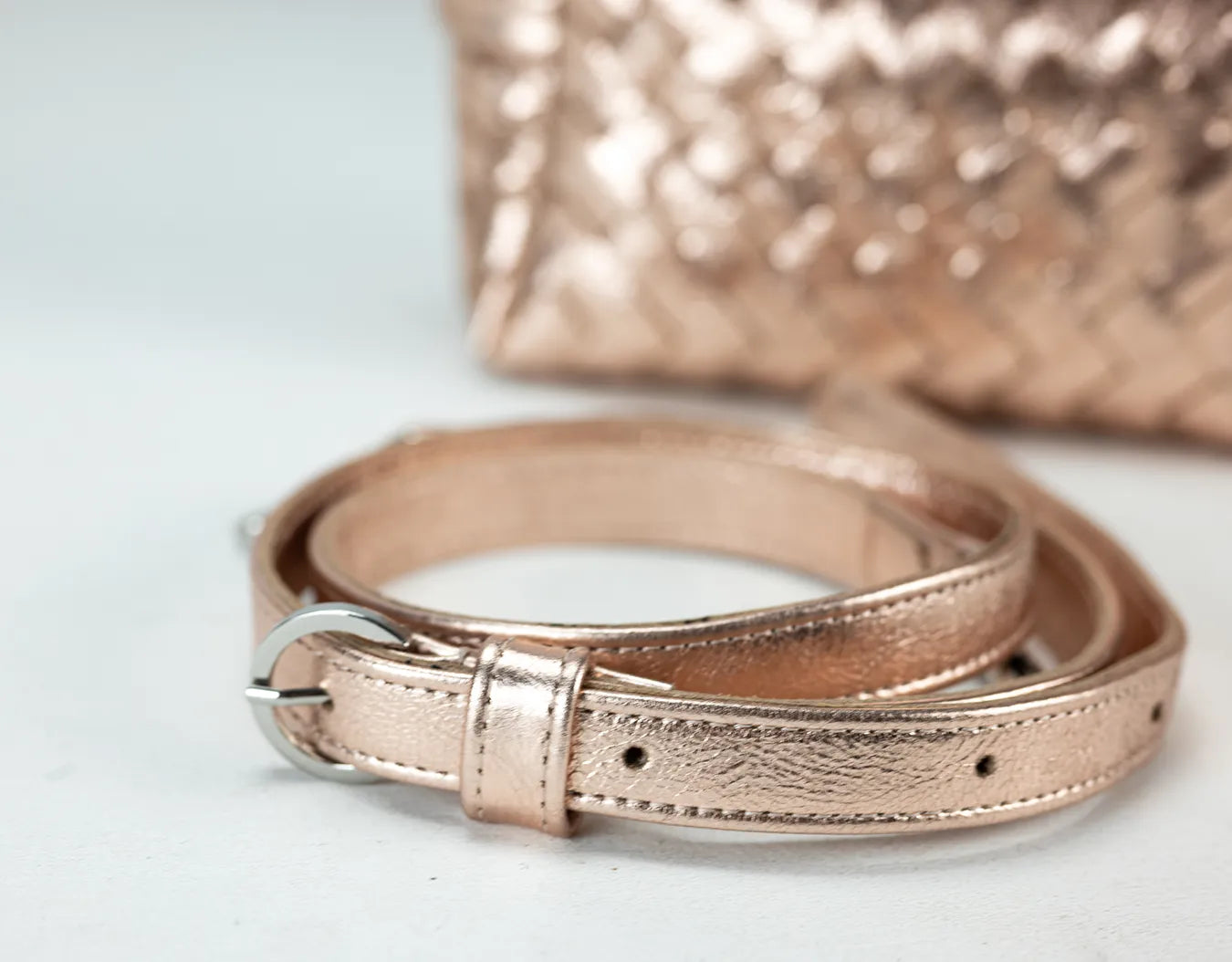 Rose gold metallic belt and handbag on a light background