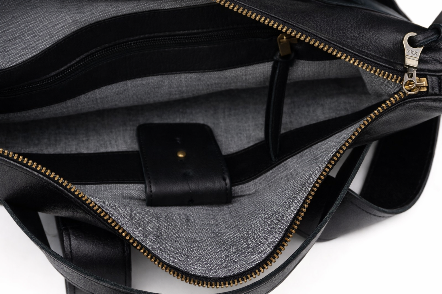 Close-up of a black leather bag with gold zipper on a white background