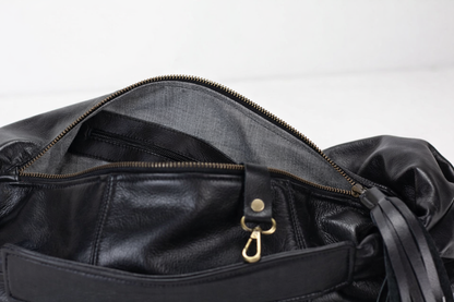 Close-up of a black leather bag with a gold zipper pull on a white background