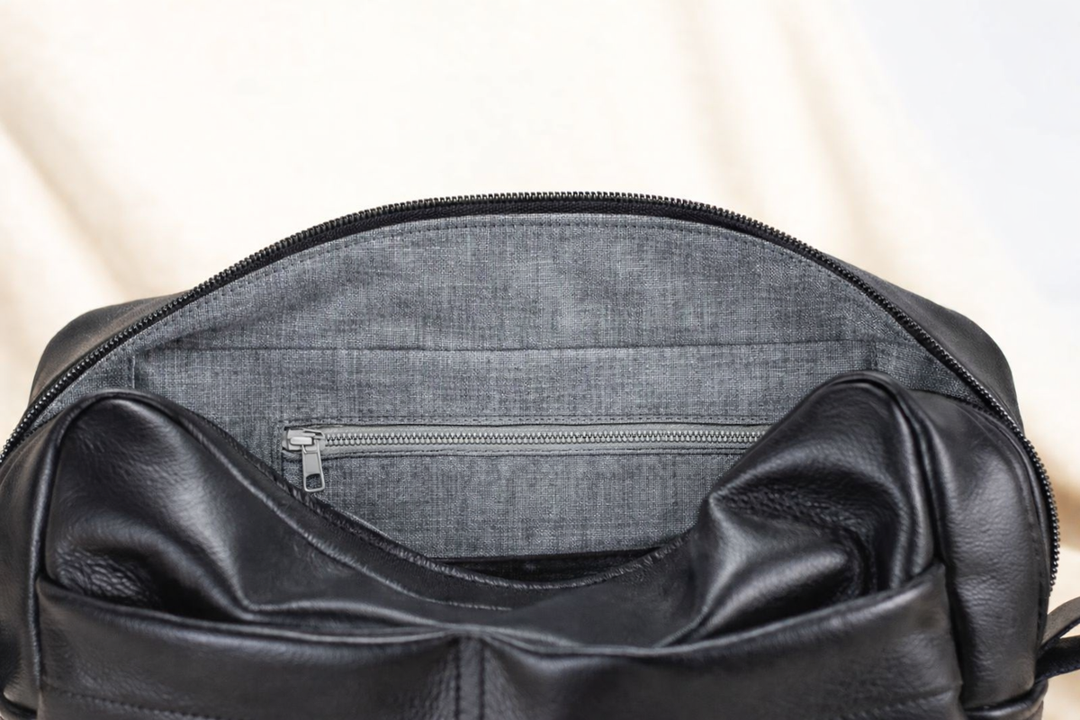 Black leather bag with zipper on a light beige background#color_black