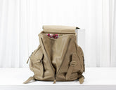 Beige backpack with floral items peeking out on a white background