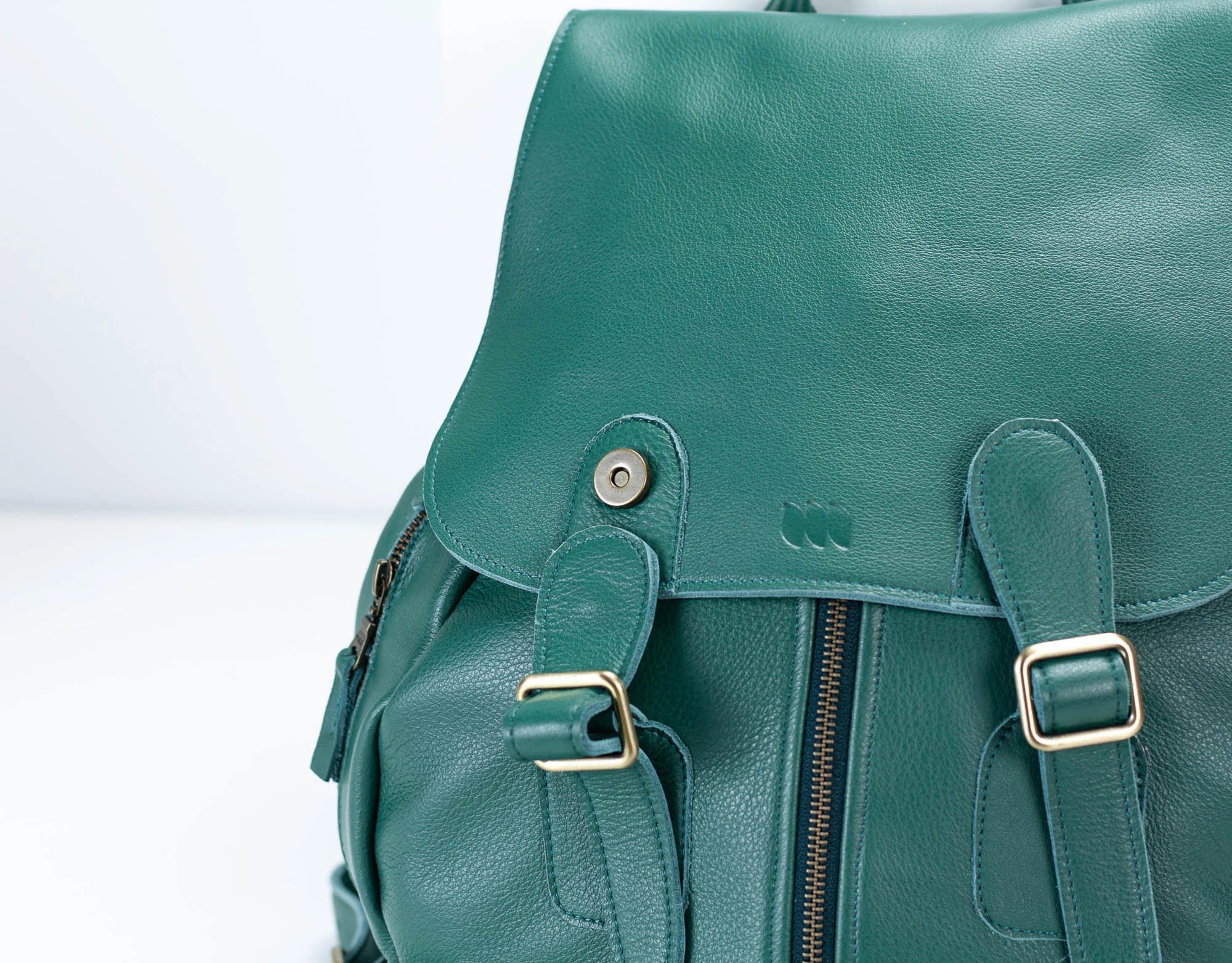 Green leather backpack with gold buckles on a light gray background