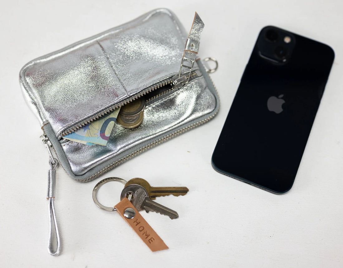 Silver wallet, keys, and black phone on a white background