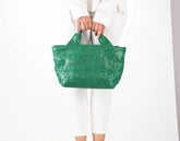 Green textured handbag held by a person wearing a white outfit on a light gray background