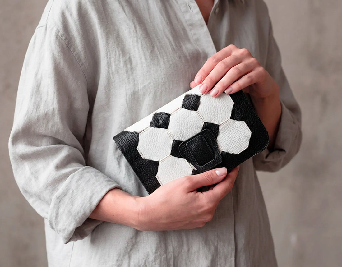 Person holding a black and white patterned clutch bag against a neutral background