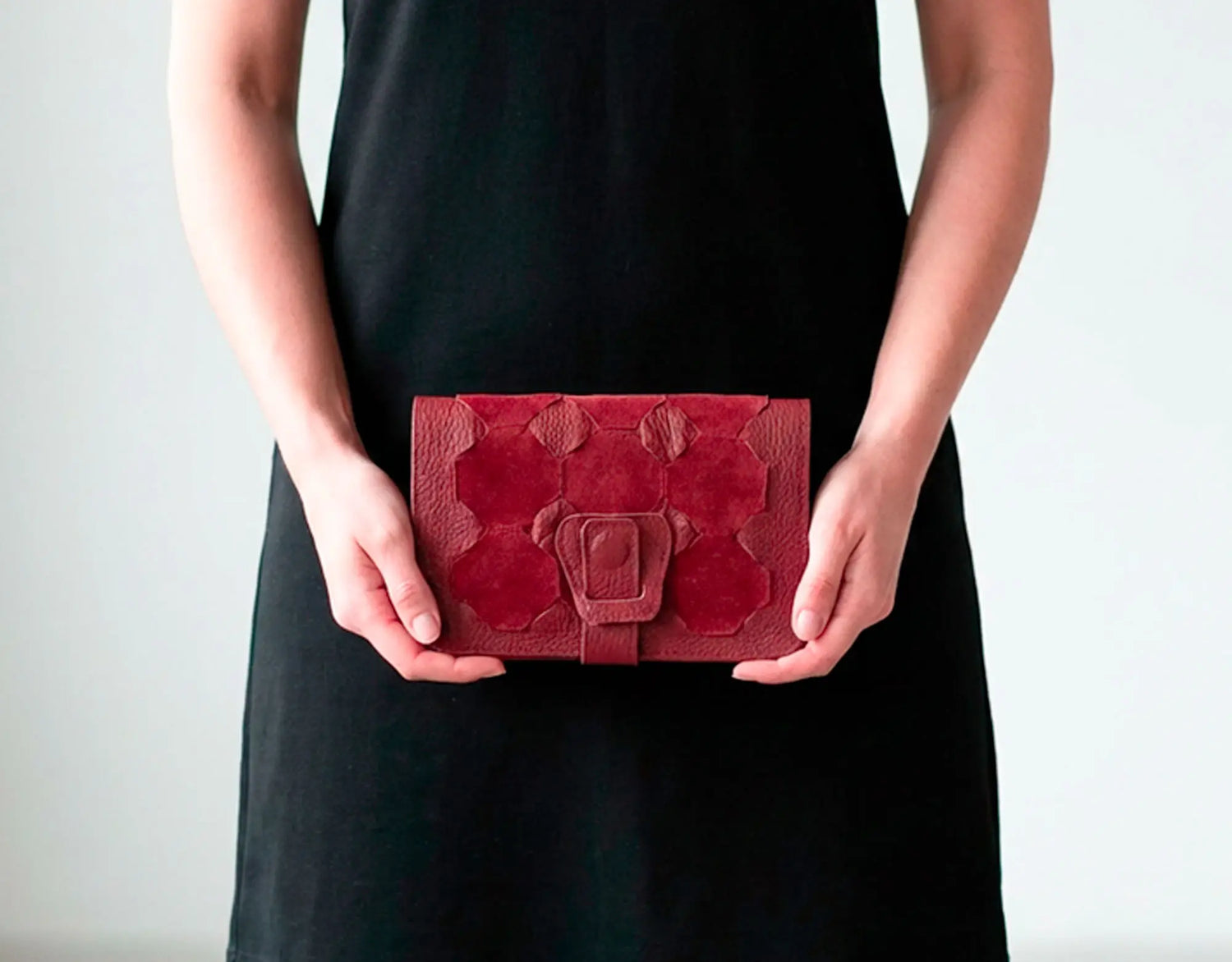 Person holding a red textured clutch bag against a plain background