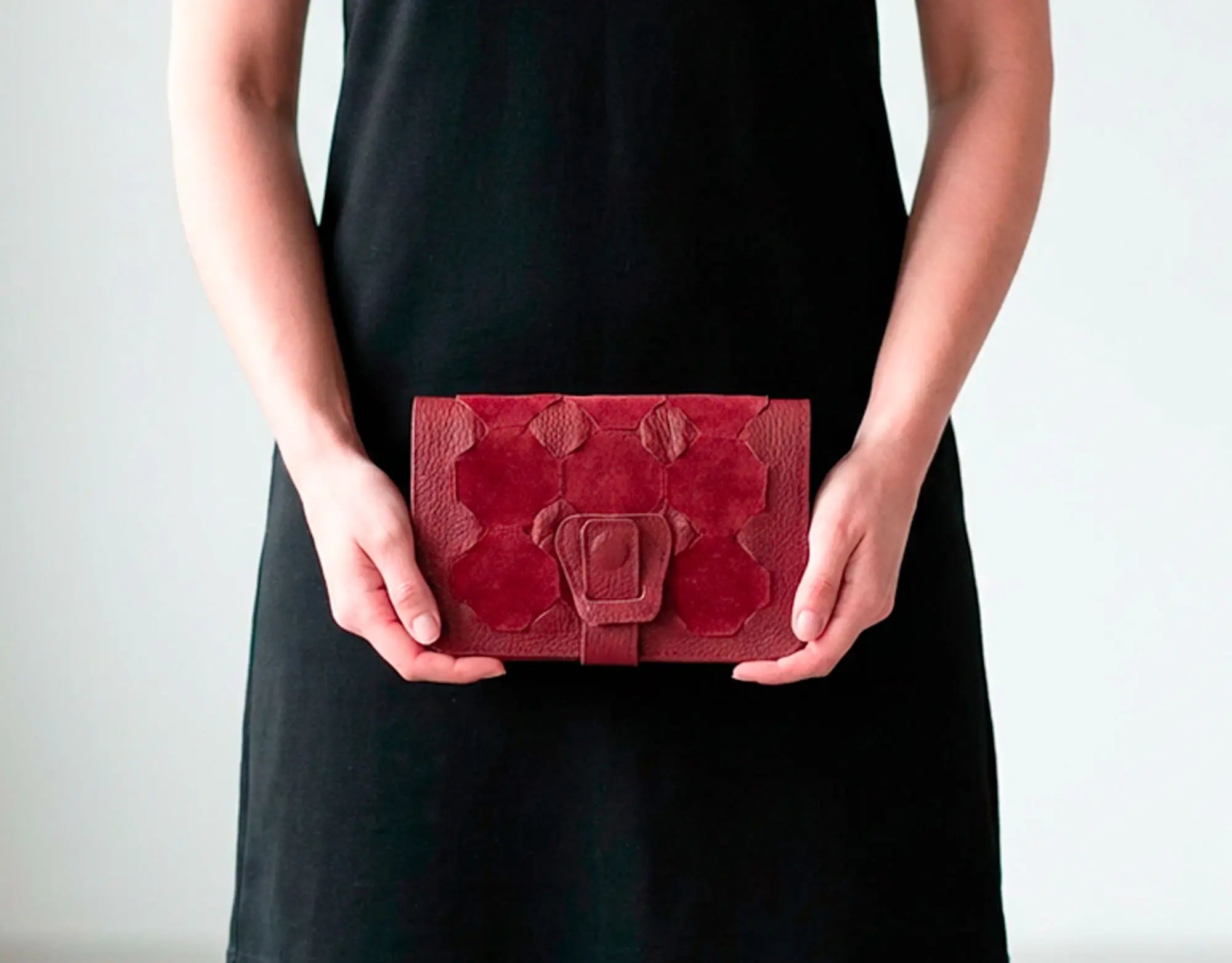 Person holding a red textured clutch bag against a plain background