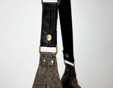 Black leather strap with gold hardware on a textured fabric background