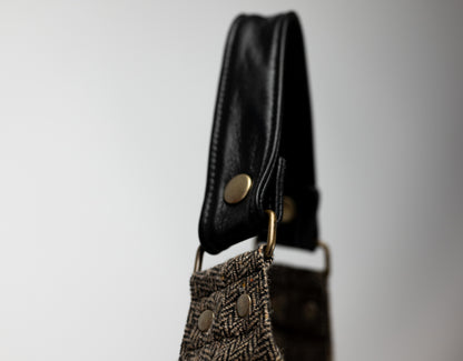 Close-up of a black leather strap with a gold buckle on a textured bag against a gray background