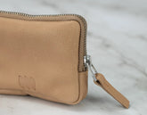 Close-up of a tan leather wallet with a zipper on a light marble background