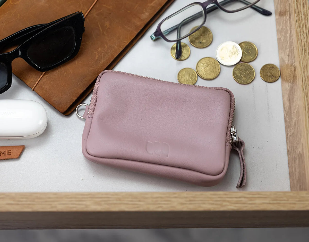 Pink wallet with sunglasses, notebook, and coins on a wooden surface#color_sandy-pink