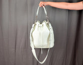 White leather handbag held by a person against a gray background