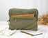 Green toiletry bag with a zipper on a white surface with a blurred natural background