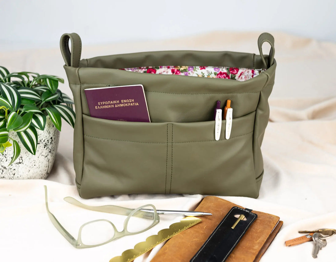 Green bag with compartments containing a passport, sunglasses, and other items on a light background.